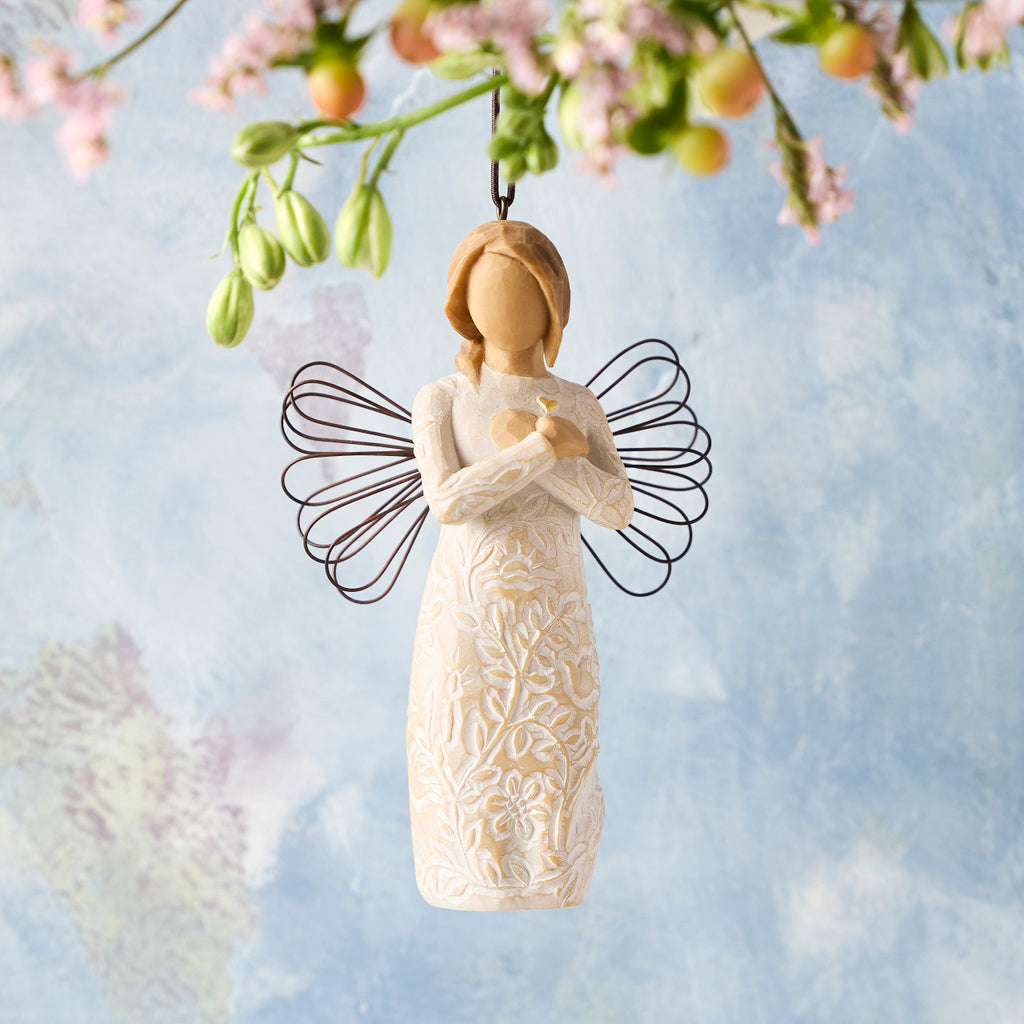 Willow Tree Remembrance Ornament, 4.5”h hand-painted resin angel figure in cream dress carved with symbols of nature, wire wings, crossed hands under small gold-leaf heart, brown elastic cord, hanging in front of sky blue painting