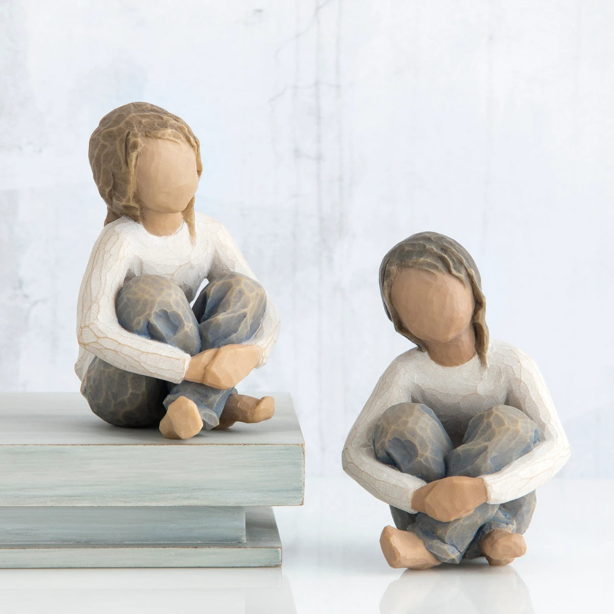 Set of two girl figurines in white shirts sitting down in blue jeans