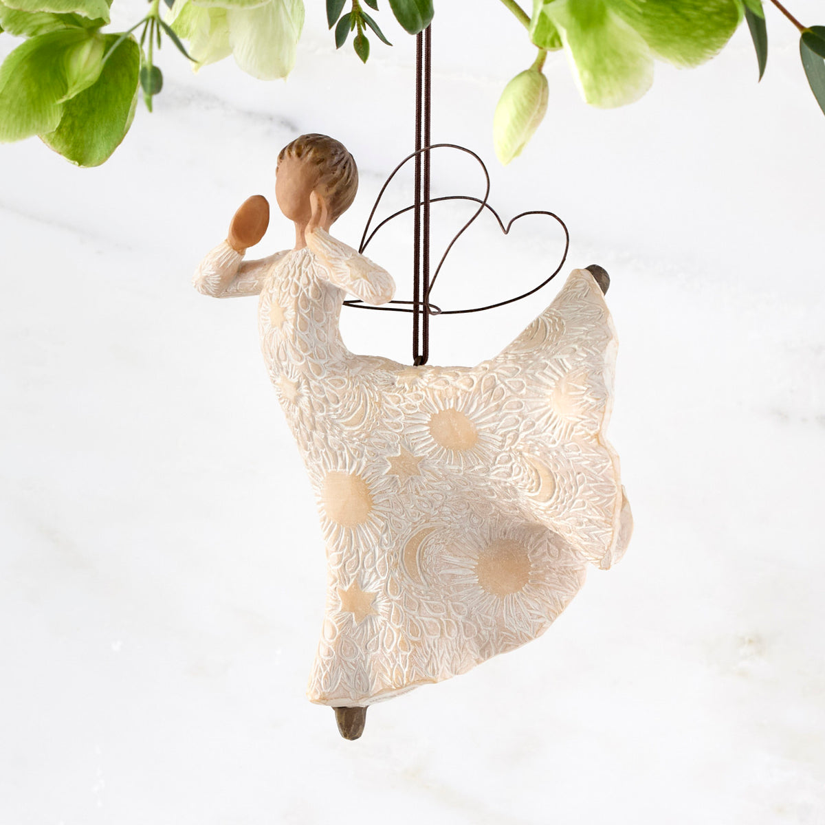 Left view of figure in cream dress carved with celestial patterns in ballet pose with hands raised to mouth and leg up behind her, wire wings on back and ornament hook on head