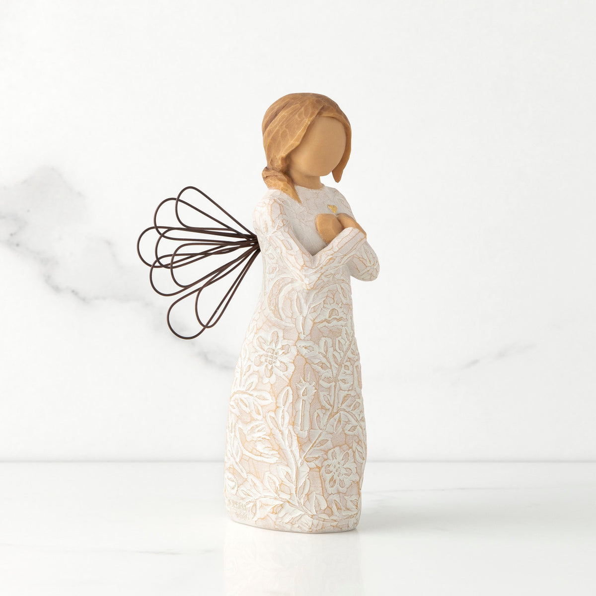 Right side view of standing female figure with wire wings in cream dress carved with natural symbols, hands crossed under gold heart on chest