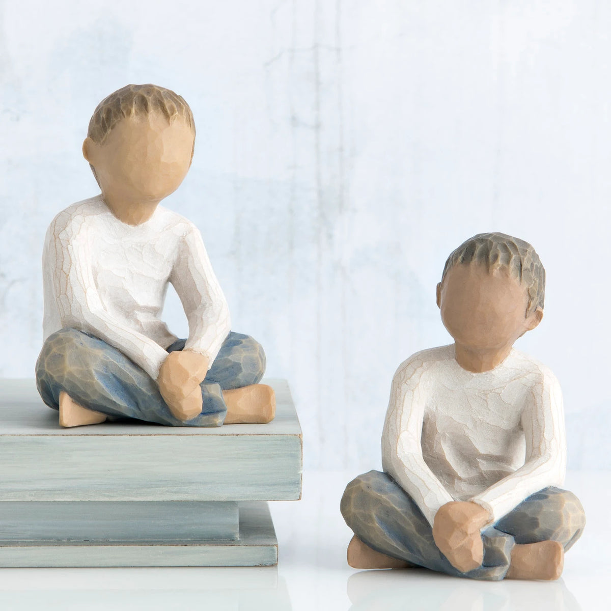 Two young boy figurines sitting next to one another in white shirts and blue jeans
