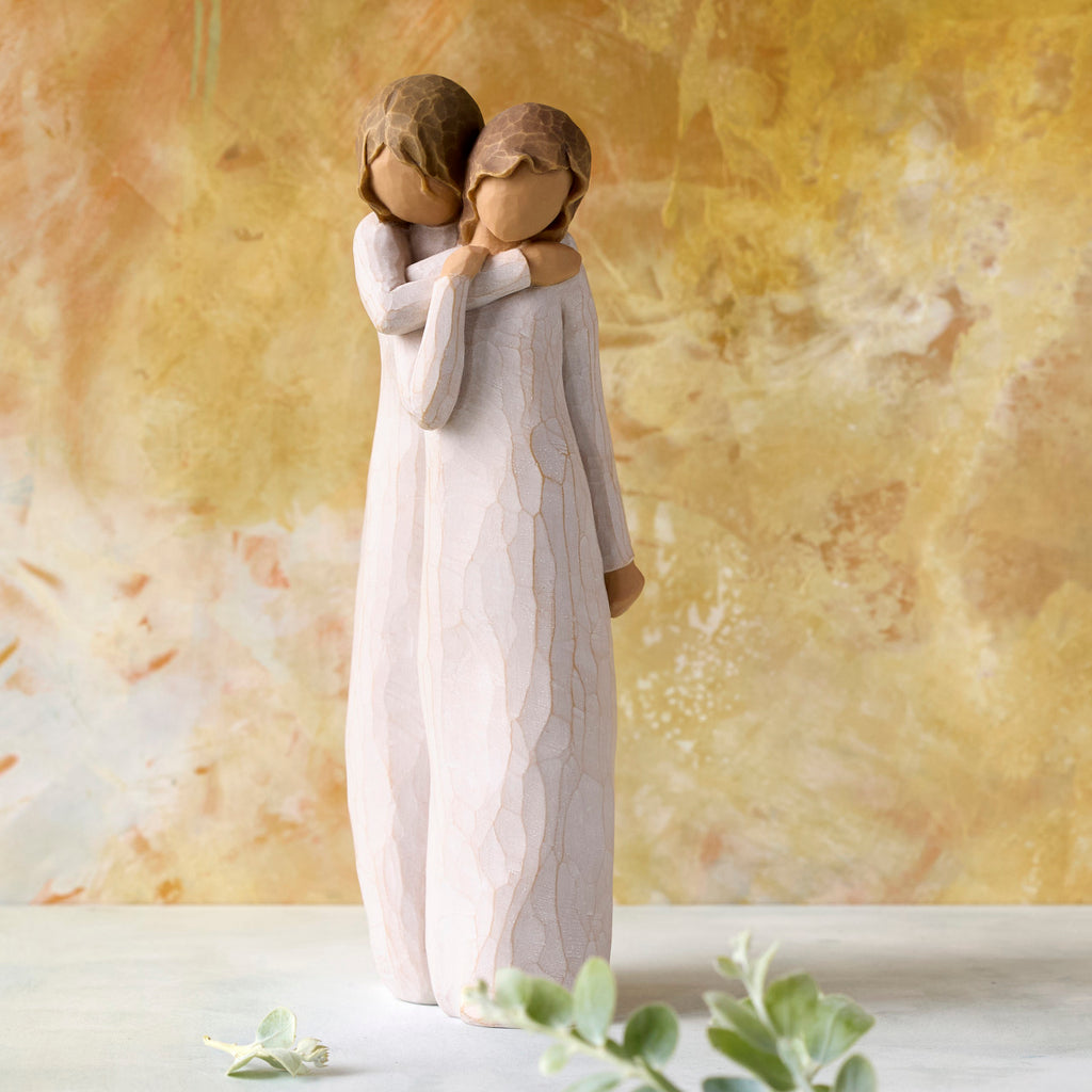 Willow Tree Chrysalis, 9”h hand-painted standing resin figure of two women in cream dresses; one standing behind and embracing the other, in front of ochre painting
