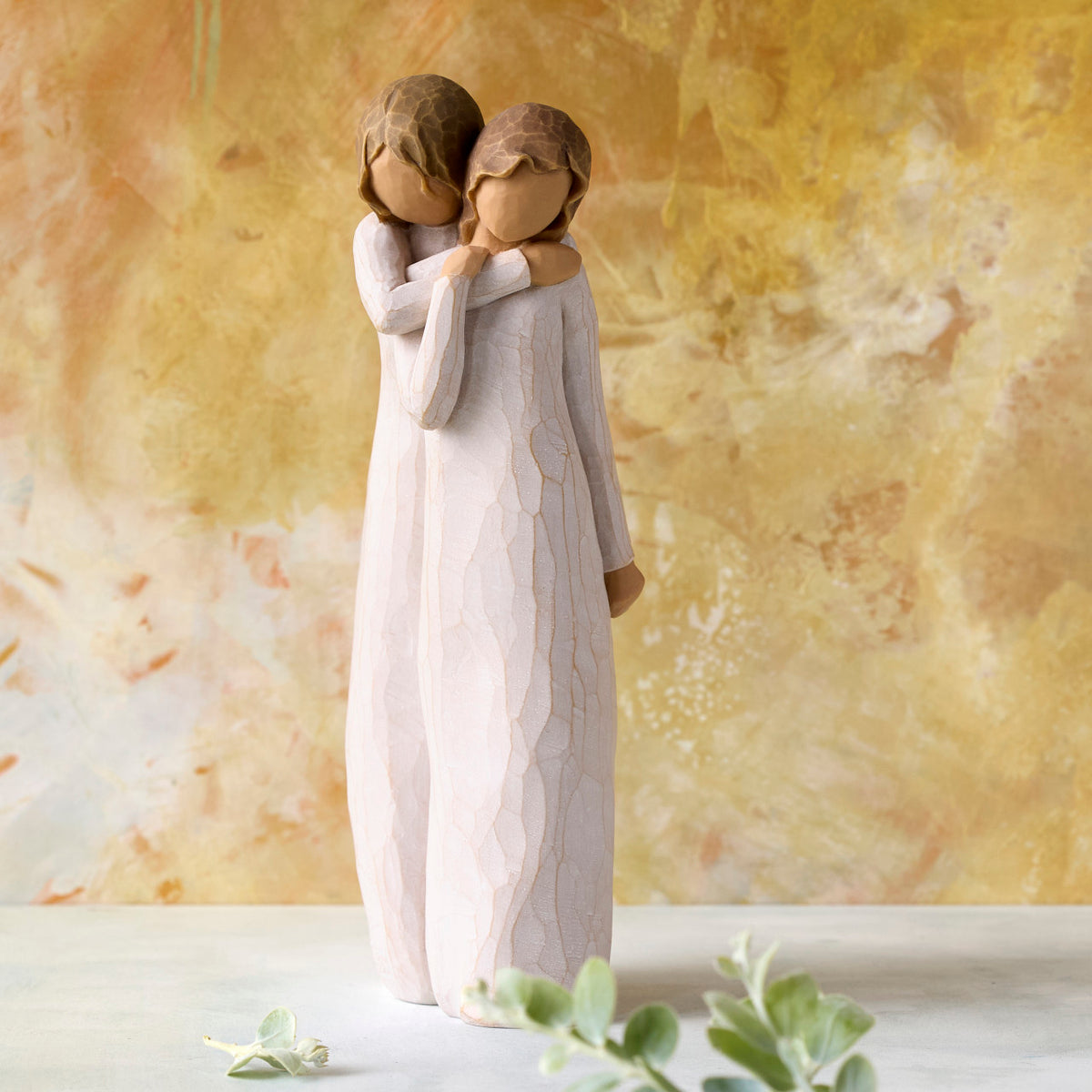 Willow Tree Chrysalis, 9”h hand-painted standing resin figure of two women in cream dresses; one standing behind and embracing the other, in front of ochre painting