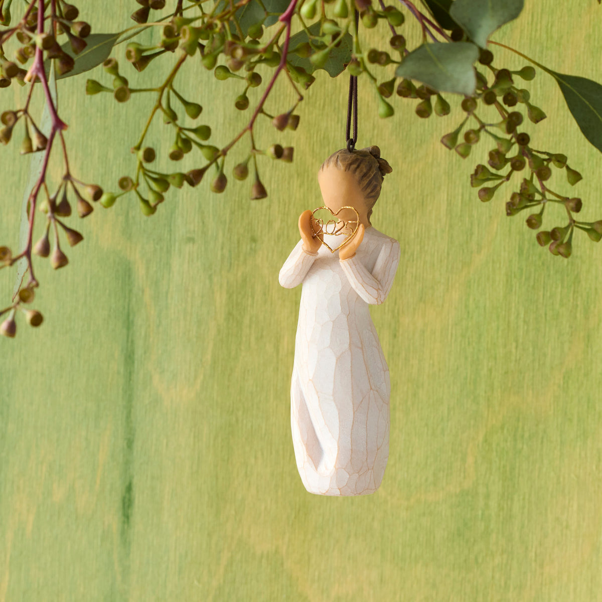 Willow Tree 2025 Ornament, 4”h hand-painted resin figure in cream dress, holding wire heart with 2025 inside, brown elastic cord, hanging in front of mossy green painting