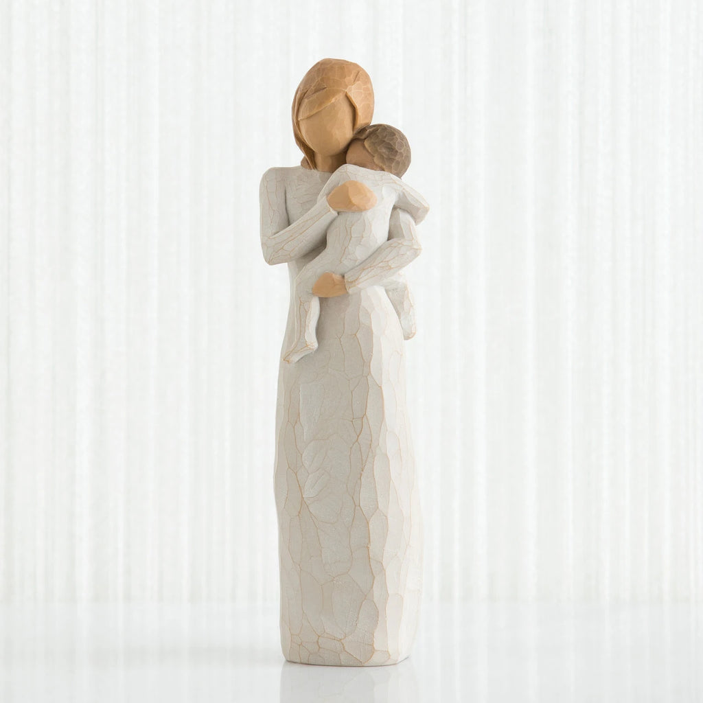 Faceless woman figurine in white dress holding brown haired baby in white clothes