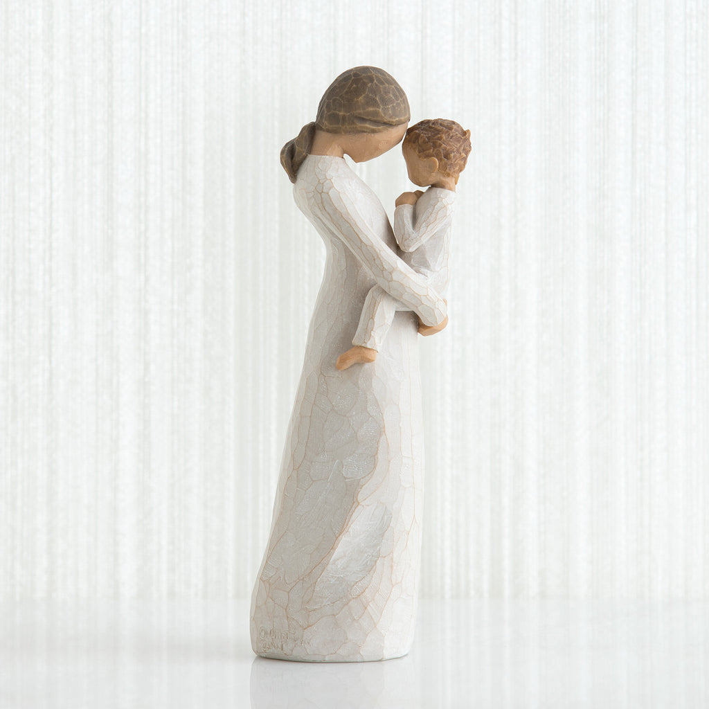 Side view of faceless mom figurine wearing white dress holding child in white outfit in her arms