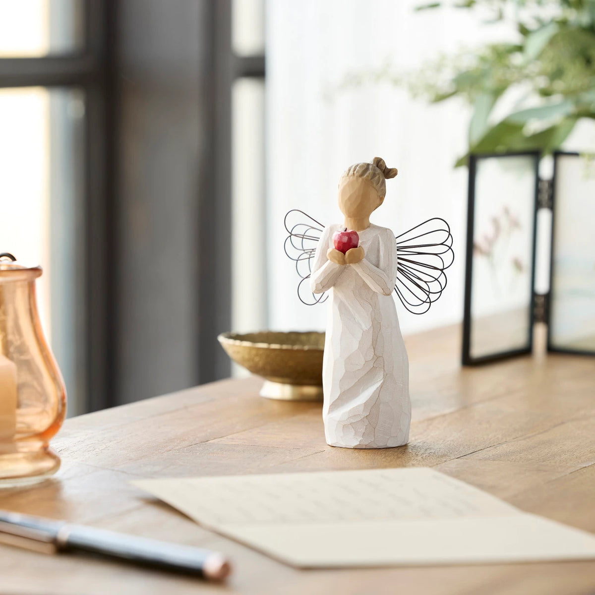 Willow Tree You're The Best!, 5.5”h hand-painted standing resin angel figure in cream dress with wire wings, holding red apple in outstretched hands, on desk with letter