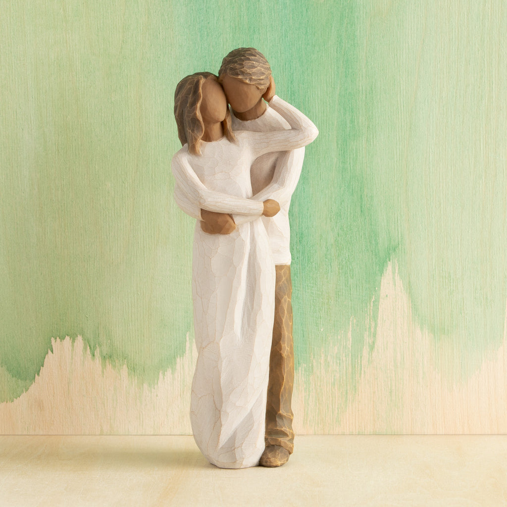 Front view of couple, standing with arms around each other. Woman and man have darker skin tones and hair color. Green painted background.