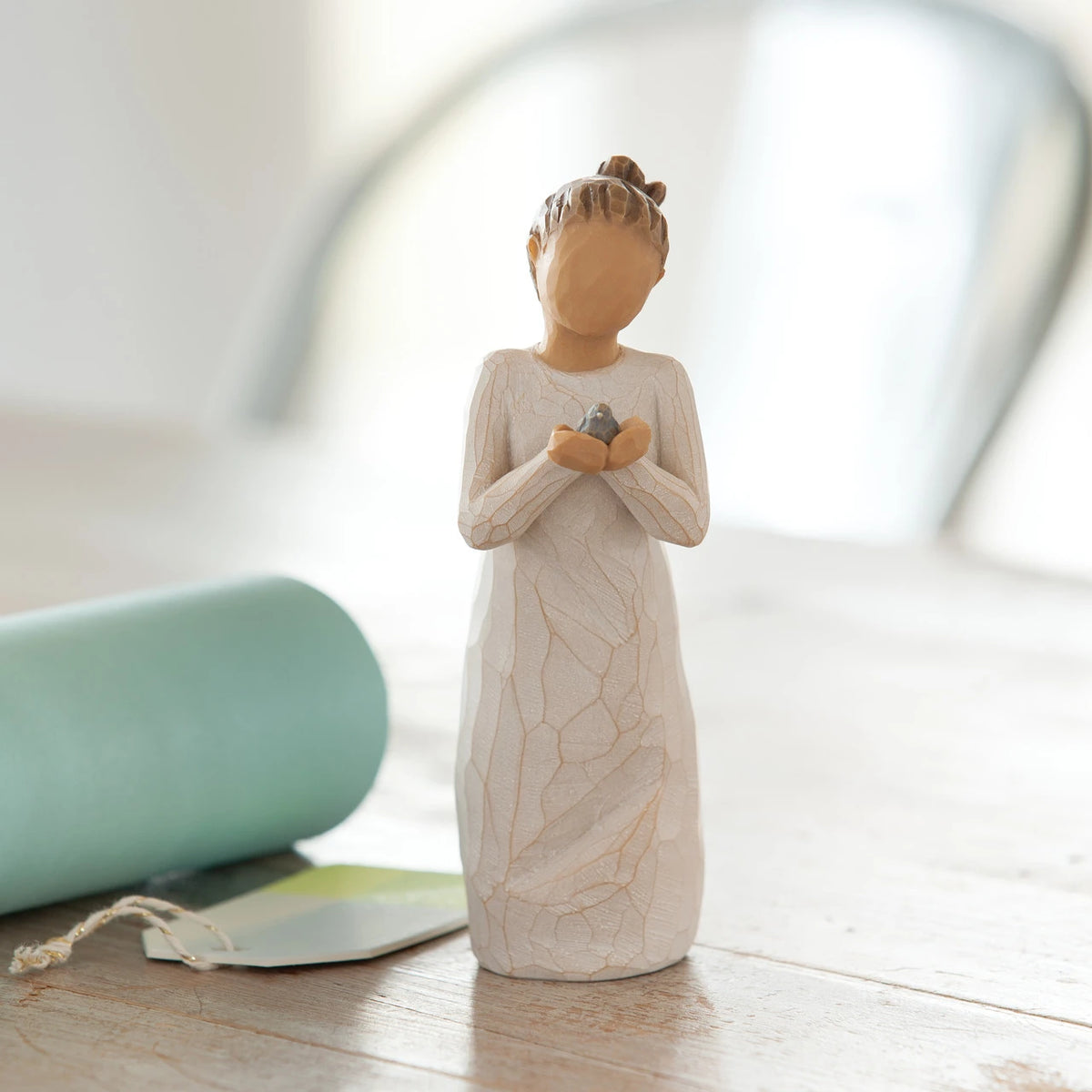 Willow Tree Nurture, 5.5”h hand-painted standing resin figure in cream dress, holding baby bluebird, on table near window