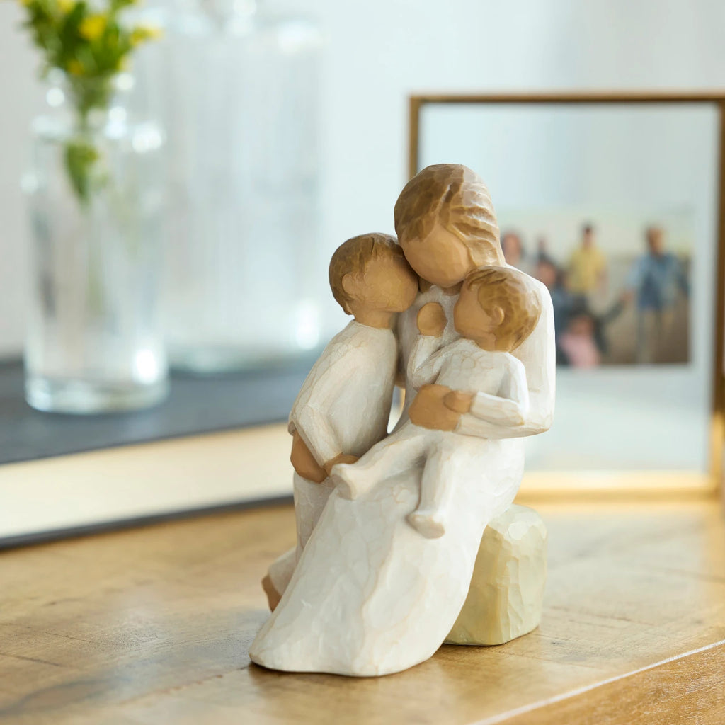 Willow Tree Quietly, 5”h hand-painted seated resin figure, one arm holding small toddler, other arm around standing older child, all in cream clothing, on table with photographs