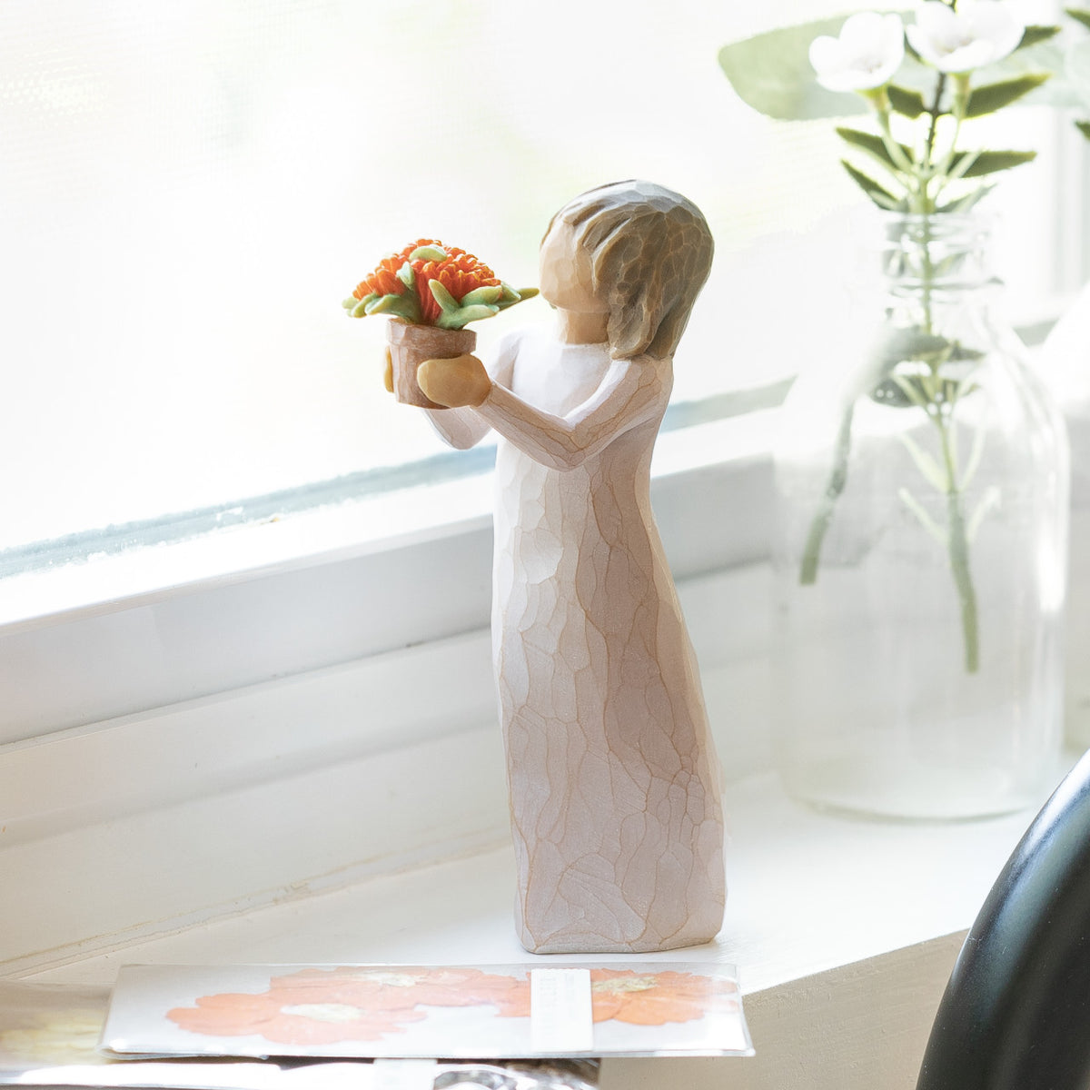 Willow Tree Little Things, 5.25”h hand-painted standing resin figure in cream dress, holding out terracotta pot with orange flowers, on bright windowsill